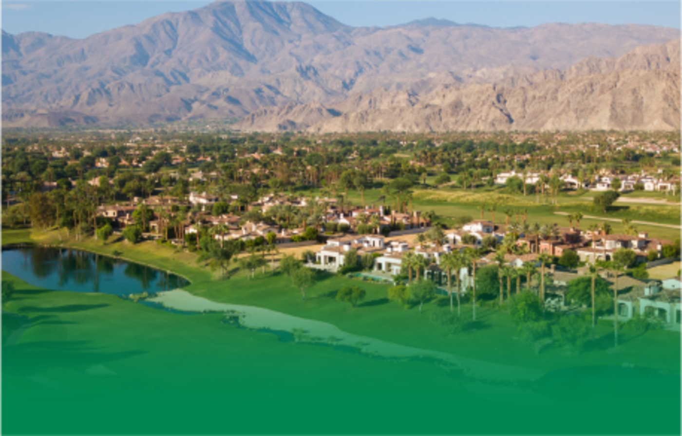 An overhead shot of La Quinta, California featuring houses, green areas and ponds with mountains in the background